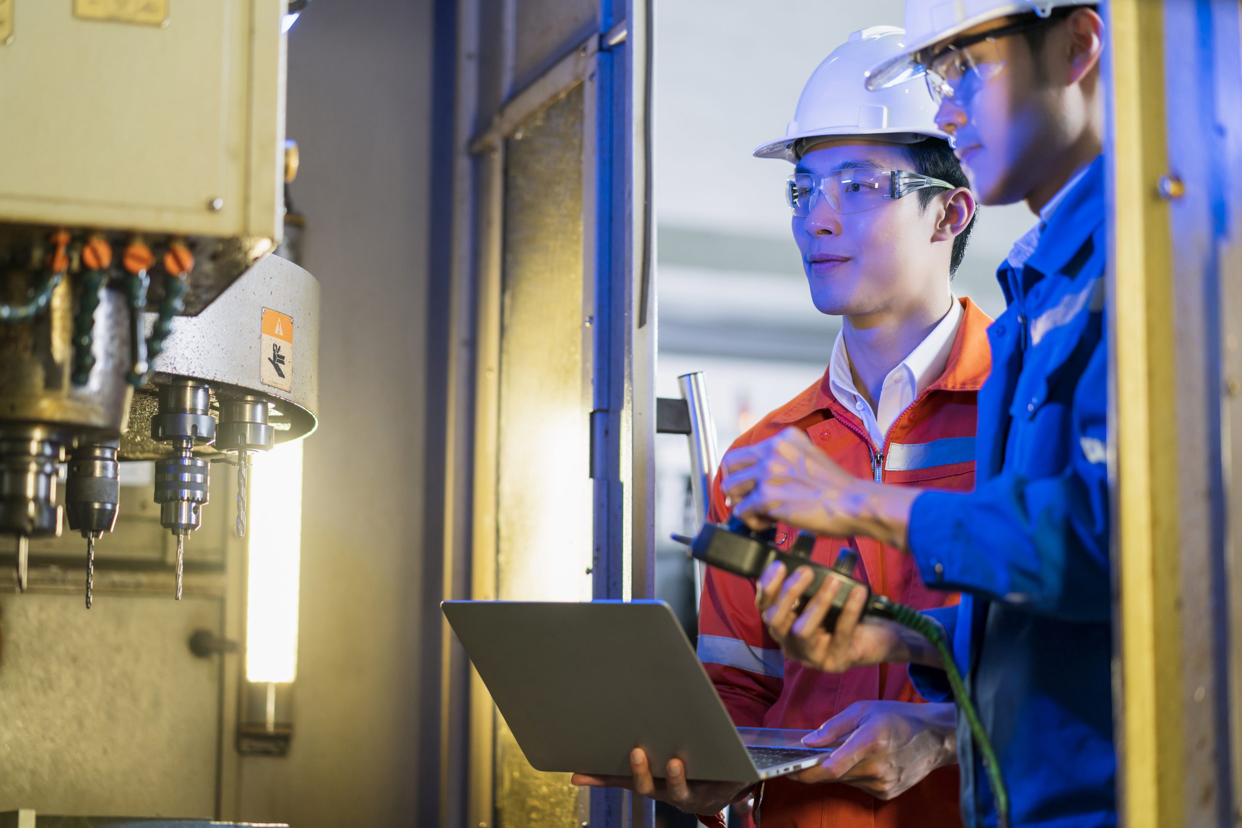 Male Asian engineer professional having a discussion standing concult cnc machine in the factory ,two asian coworker brainstorm explaining and solves the process of the cnc operate machine