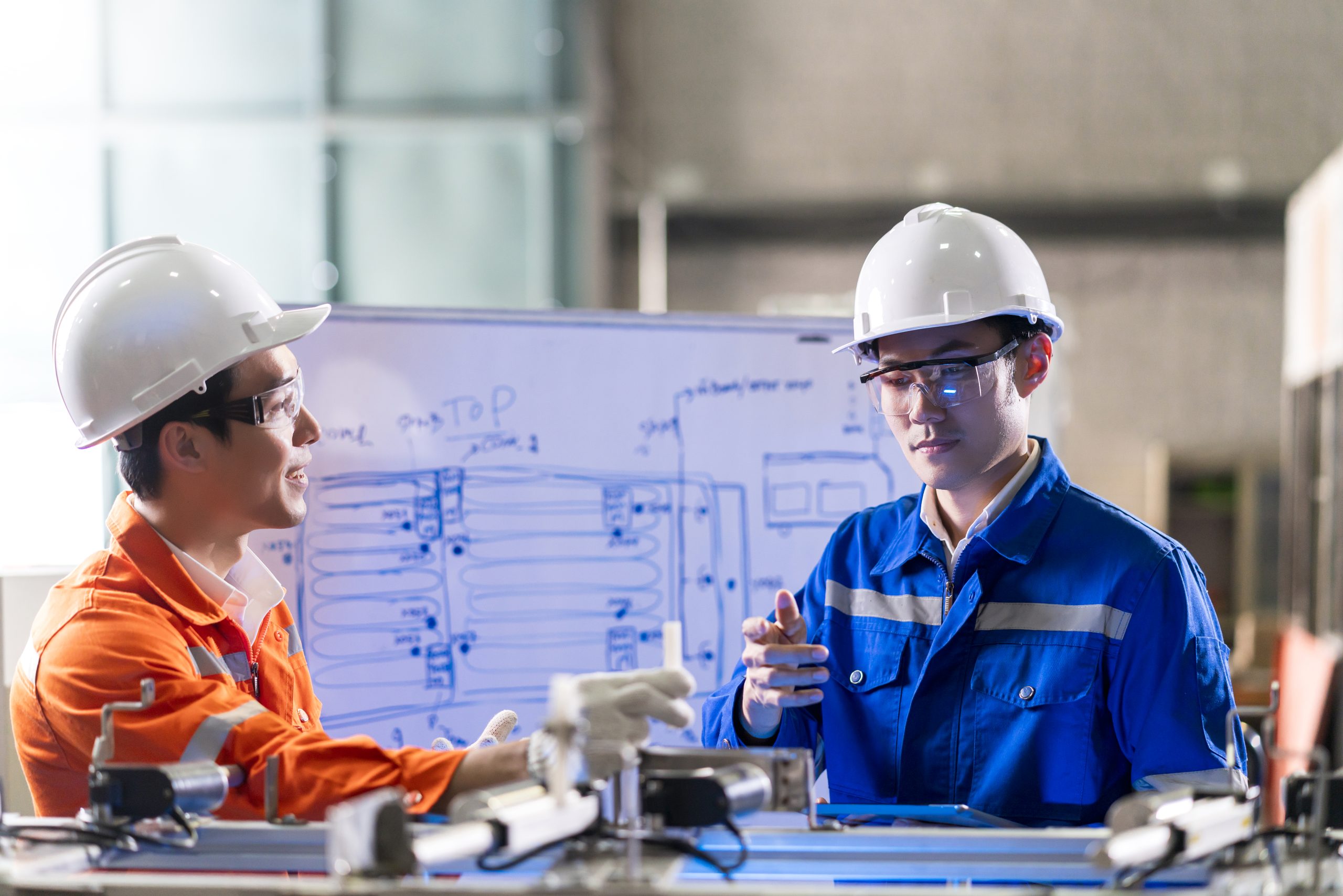 Male Asian engineer professional having a discussion standing by the machine in the factory ,two asian coworker brainstorm explaining and solves the process curcuit mother board of the machine