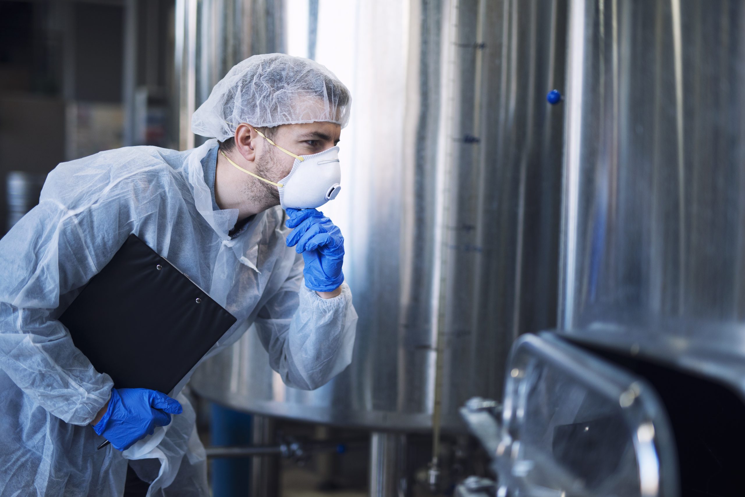 Factory worker in white protective uniform with hairnet and mask looking at parameters of an industrial machine.