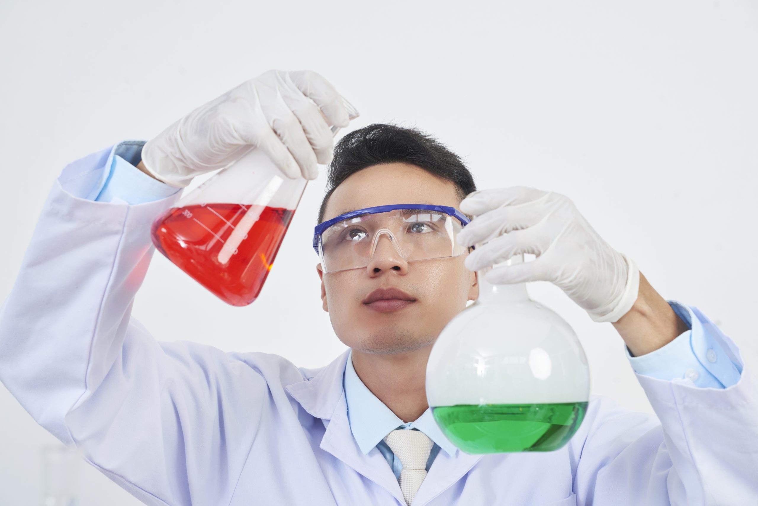 Young Asian chemist holding two flasks with red and green liquids