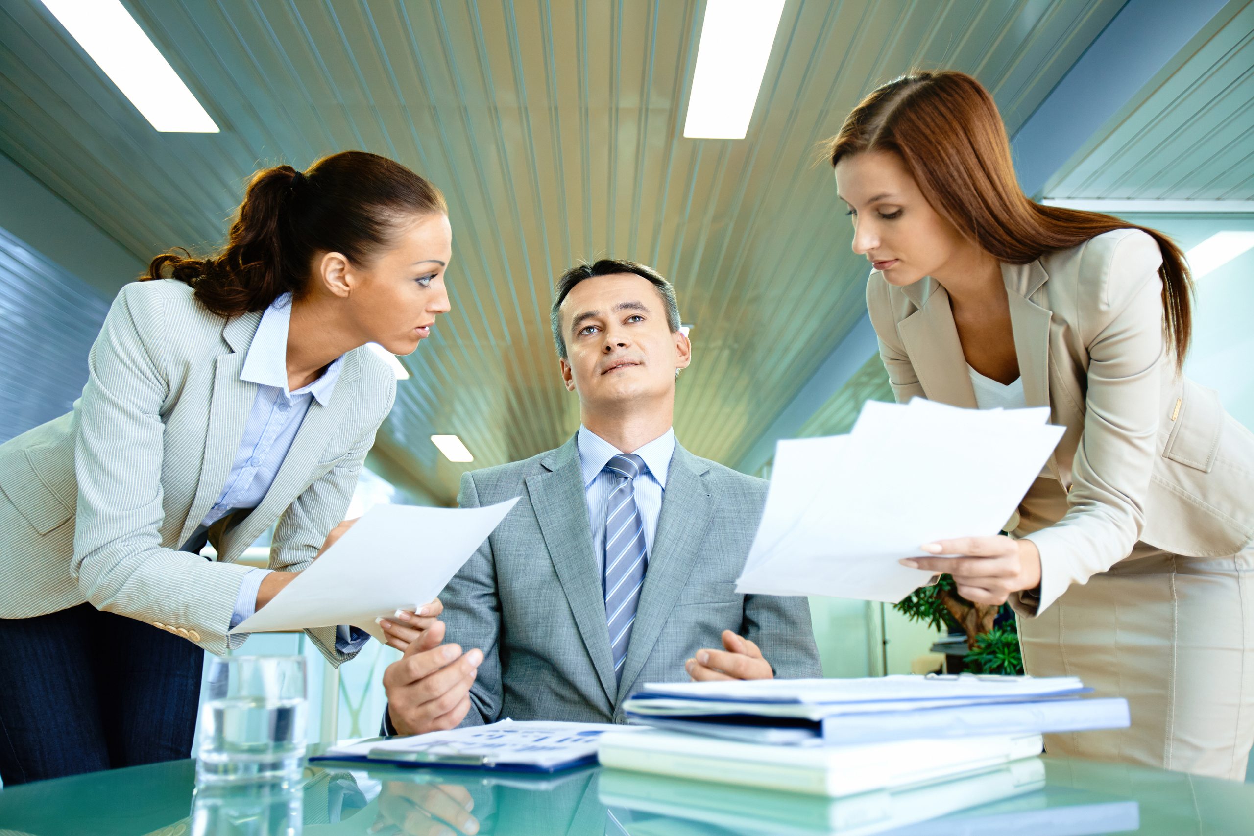 Inspirated boss sitting at workplace surrounded by two secretaries with papers