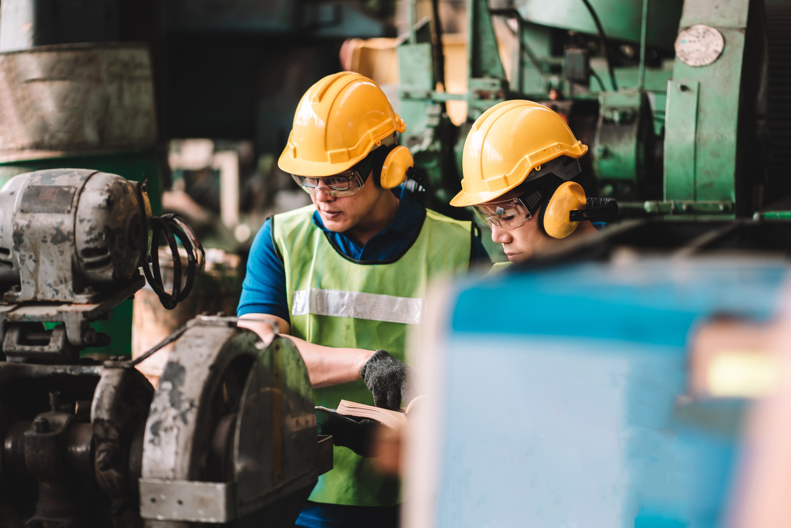 Work at factory.Two Asian workers man team working together in safety work wear with yellow helmet using Manual book.in factory workshop industry meeting professional